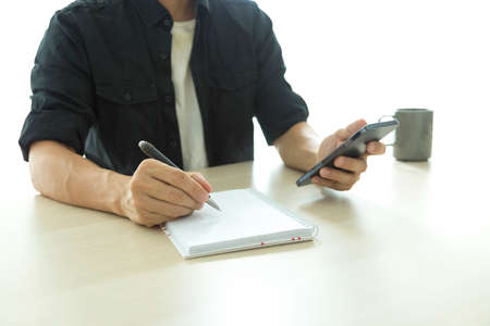 Young man writing and working on digital mobile smartphone, coffee cup on desk at cafe restaurant, work from home, digital technology, internet, online business concept.の写真素材