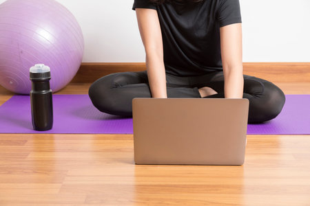 Young woman watching live online pilates group class tutorial on laptop computer at home, doing yoga...