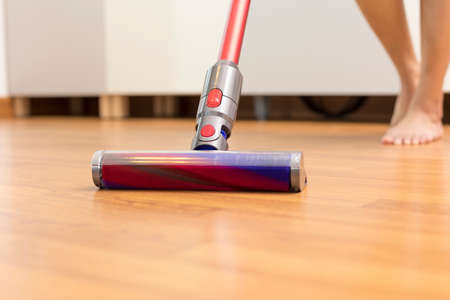 Lower section of woman vacuuming hardwood floor at homeの写真素材