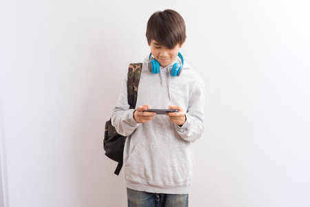 Asian teen boy schooler texting or playing game online on smartphone isolate on white background.