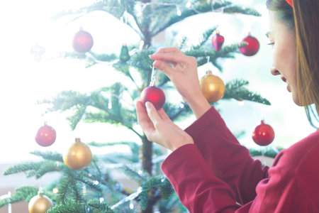 Asian woman decorates the Christmas tree with Christmas ball. Female hand decorates a Christmas tree...