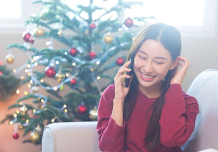 Happy young Asian woman talking on phone with friend during Christmas season.の写真素材
