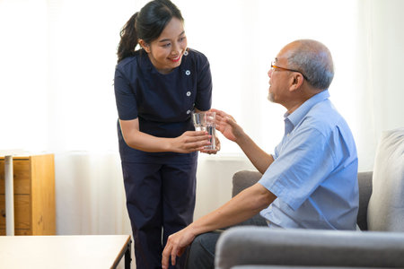 Smiling nurse giving glass of water to senior asian man in nursing home or assisted living facility.の写真素材