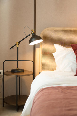 Modern bedroom room with stylish comfortable red, brown and yellow pillow on it. Side table lamp.