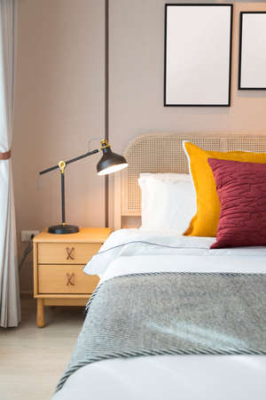 Modern bedroom room with stylish comfortable red, brown and yellow pillow on it. Side table lamp.の写真素材