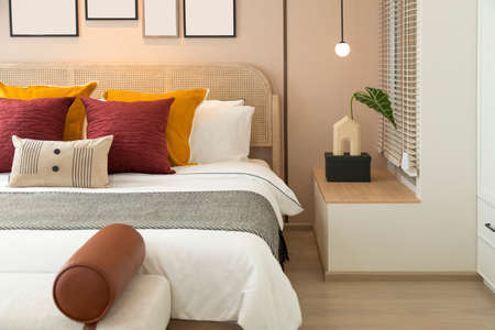 Modern bedroom room with stylish comfortable red, brown and yellow pillow on it. Side table lamp.の写真素材