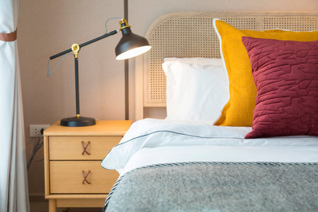 Modern bedroom room with stylish comfortable red, brown and yellow pillow on it. Side table lamp.の写真素材