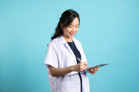 Asian doctor woman in medical uniform and clipboard smiling at camera standing on blue white...