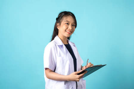 Asian doctor woman in medical uniform and clipboard smiling at camera standing on blue white background.の写真素材