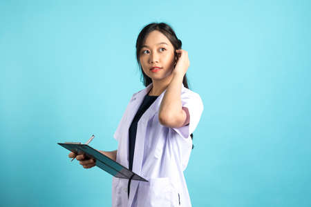 Asian doctor woman in medical uniform and clipboard smiling at camera standing on blue white background.の写真素材
