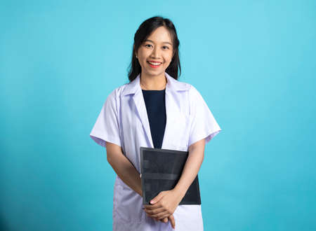 Asian doctor woman in medical uniform and clipboard smiling at camera standing on blue white background.の写真素材