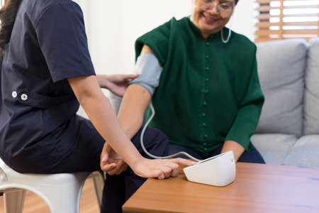 Asian woman nurse at nursing home taking care of senior man. Caregiver Therapist doctor examining an older man use blood pressure gauge.の写真素材