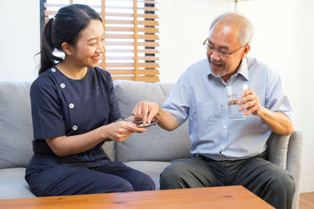 Female asian nurse takes care of sick senior man, help to remind to take a pill.の写真素材