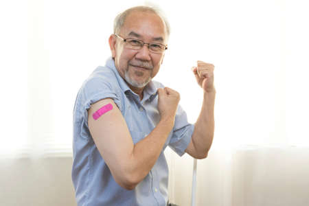 Portrait of an elderly asian man smiling after receiving the vaccine. A mature man shows his arm with a bandage after full vaccination.の写真素材