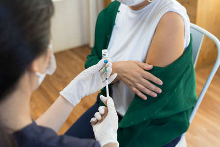 Nurse or doctor giving shot to senior female patient. Retired woman with medical face mask getting flu or  vaccine injection in her arm.の写真素材