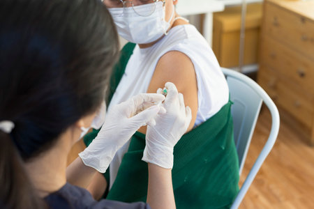 Nurse or doctor giving shot to senior female patient. Retired woman with medical face mask getting...