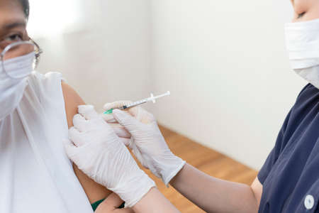 Nurse or doctor giving shot to senior female patient. Retired woman with medical face mask getting flu or  vaccine injection in her arm.の写真素材
