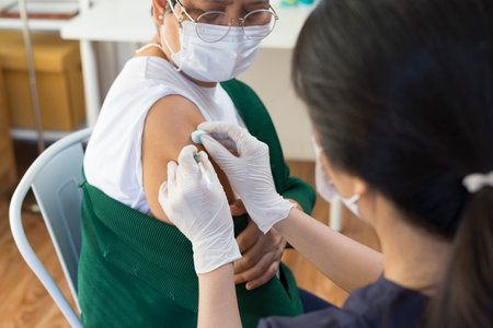 Nurse or doctor giving shot to senior female patient. Retired woman with medical face mask getting flu or vaccine injection in her arm.の写真素材