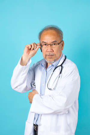 portrait of senior Asian doctor with serious face standing on blue background.の写真素材