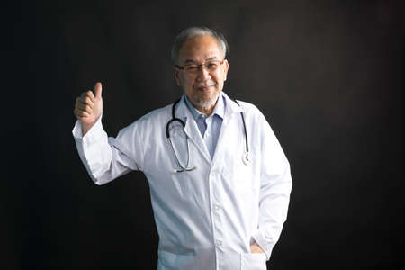 Asian doctor with stethoscope around his neck with thumb up hand stand on black background.の写真素材