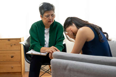 Asian psychologist doctor having session with young depressed woman in clinic. Psychology and mental therapy concept.の写真素材