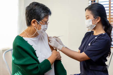 Elderly Asian woman getting coronavirus vaccine by nurse. Medical worker prepare syringe.の写真素材