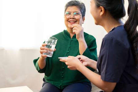 Asian nurse help to remind old Asian woman to take a pill.の写真素材