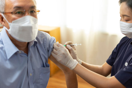 Medical worker perform a vaccine injection to senior Asian man in clinic or medical facility.