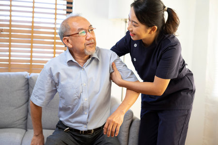 Medical assistance. Asian female nurse help Senior asian man getting up from the sofa while staying...