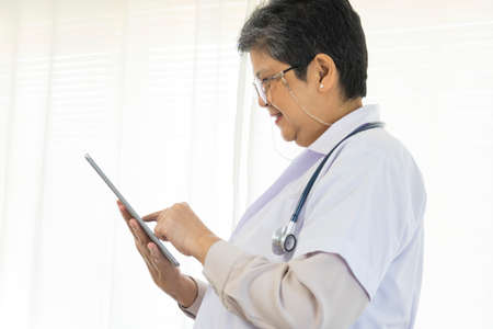 Confident senior female doctor using tablet computer standing in clinic.の写真素材