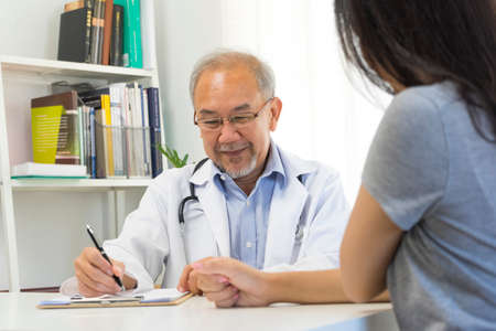 Old doctor in professional uniform examining young patient woman at hospital or medical clinic. Health care , medical and doctor staff service concept.の写真素材