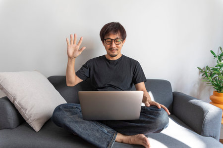 Adult handsome man making video call with friends via laptop while sitting on sofa at his modern...