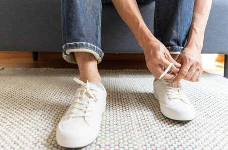 Man tie the shoelace of white sneakers sit on wood bench at home.