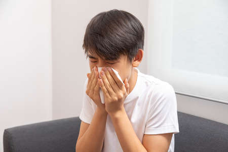 Sick Asian preteen boy blowing nose and sneeze at home, healthcare concept.の写真素材