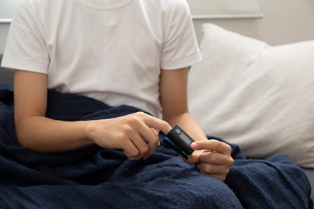 Sick asian teen boy with pulse oximeter on his finger. Ill child lying on sofa with blanket in living room.の写真素材