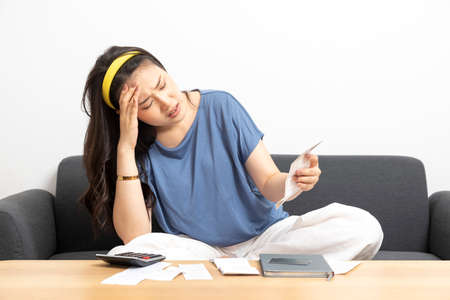 Young asian woman calculating household expenses and finance, feel frustrated at home, girl worried about debt and tax.の写真素材