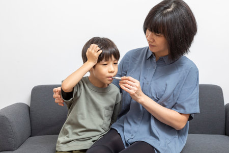 Asian woman and her son using digital thermometer on sofa at homeの写真素材