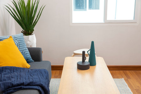 Modern interior of living room with blue and yellow pillows on grey sofa. blue blanket and green...