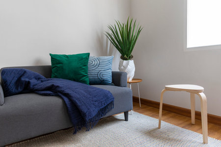 Scandinavian interior decoration of grey sofa with blue and green pillow on it. Green plant pot on...