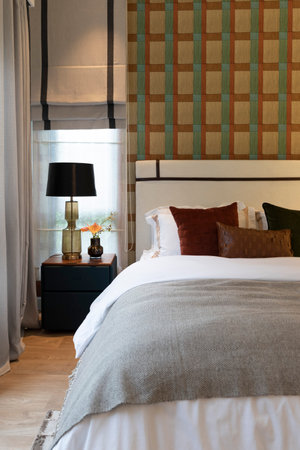 stylish bedroom interior design with wallpaper and black patterned pillows on bed and decorative table lamp.の写真素材