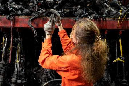 A young female mechanic works in a car repair shop. The girl is dressed in an orange jumpsuit.