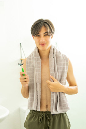 Young teen boy with a towel over his shoulder and a shaving razor in bathroom.