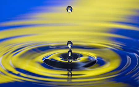 drop of water hitting a pool of water with color backgroundの写真素材