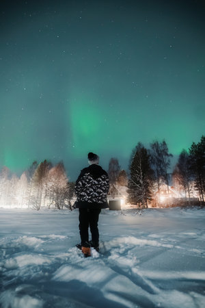 Man stood in snow in front of house under northern lights in Rovaniemi, Laplandの写真素材
