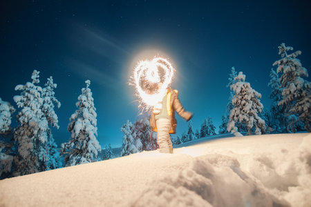 Girl with sparkler on snowy hill in winter forest in Rovaniemi, Laplandの写真素材