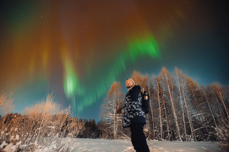 Man stood in snow looking up at strong northern lights in Rovaniemi, Laplandの写真素材