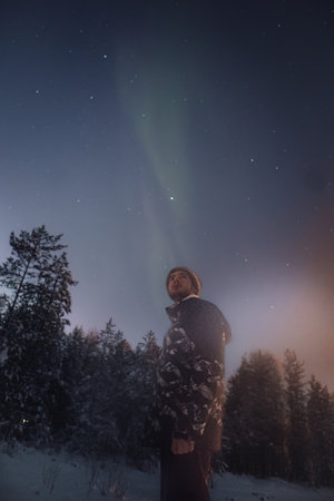 Man stood in snow in Lapland under faint aurora in starry sky in Rovaniemiの写真素材