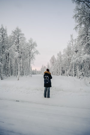 Girl in black coat stood in snow taking photos in Rovaniemi, Laplandの写真素材