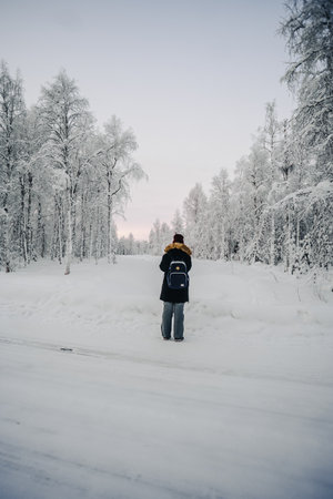 Girl in black coat stood taking photos of snowy forest in Rovaniemi, Laplandの写真素材