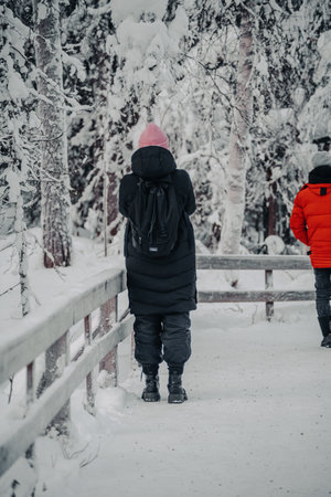 Woman in black coat taking photos in snowy forest in Ranua, Laplandの写真素材